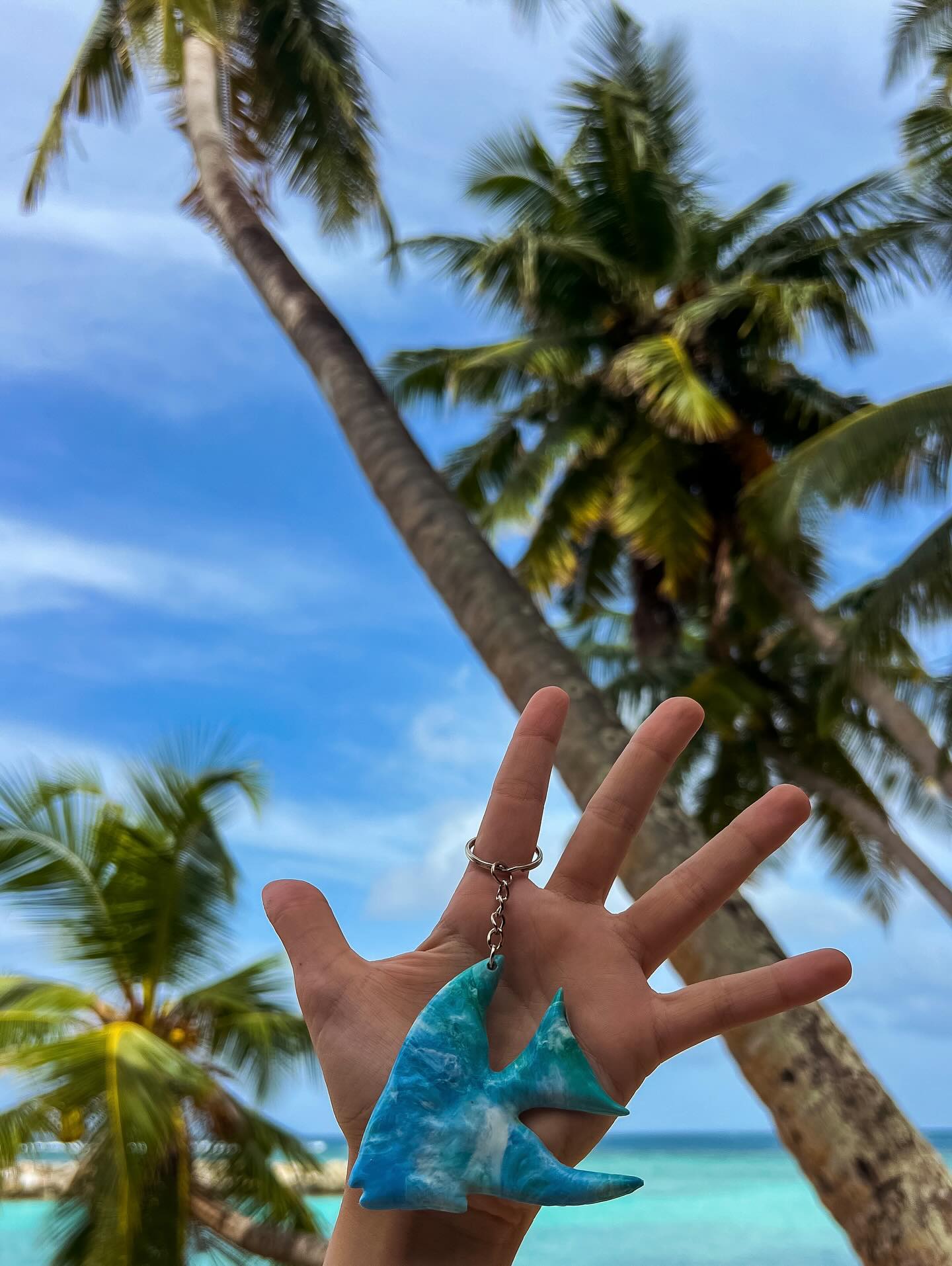 Hand holding recycled plastic fish keychain with tropical palms and sea in background